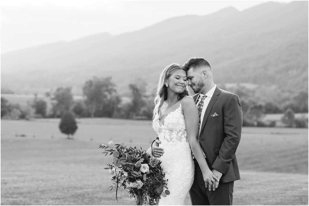 Bride poses with groom looking over her shoulder. Image in black and white with Hiltons VA crooked river venue in background.