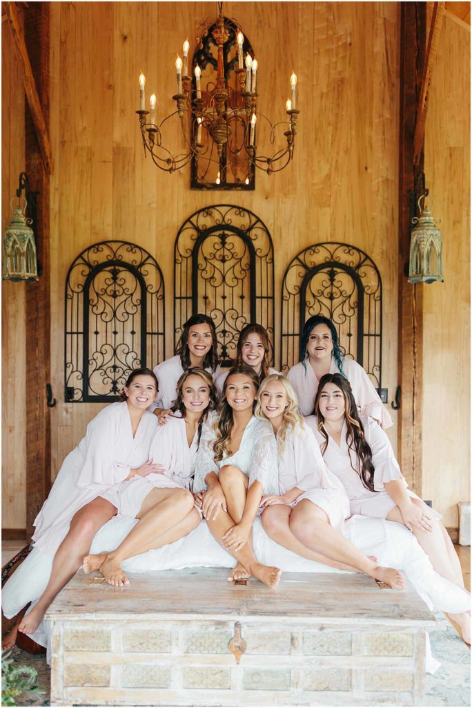Bride posing with bridesmaids sitting on bed at the tobacco barn at crooked river wedding venue