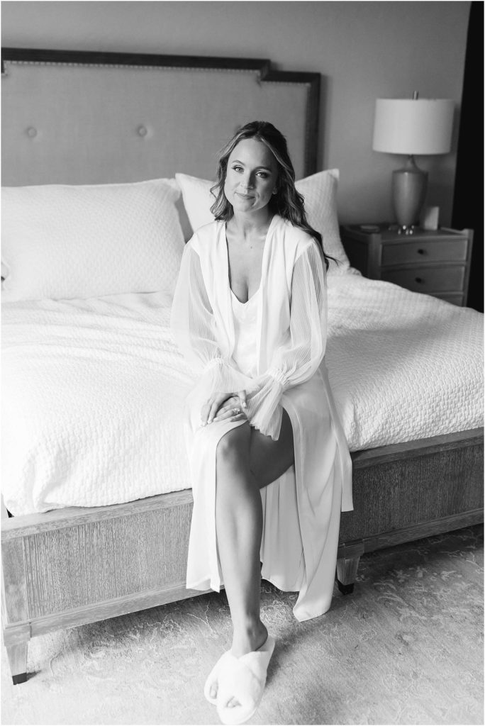 Bride in robe sitting on bed smiling for Chateau Selah photographer