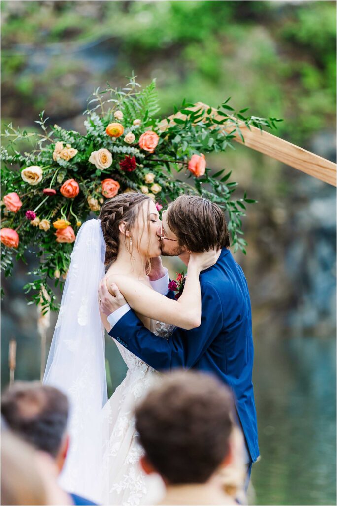 Bride and groom first kiss in front of susan liles florist decorated arbor