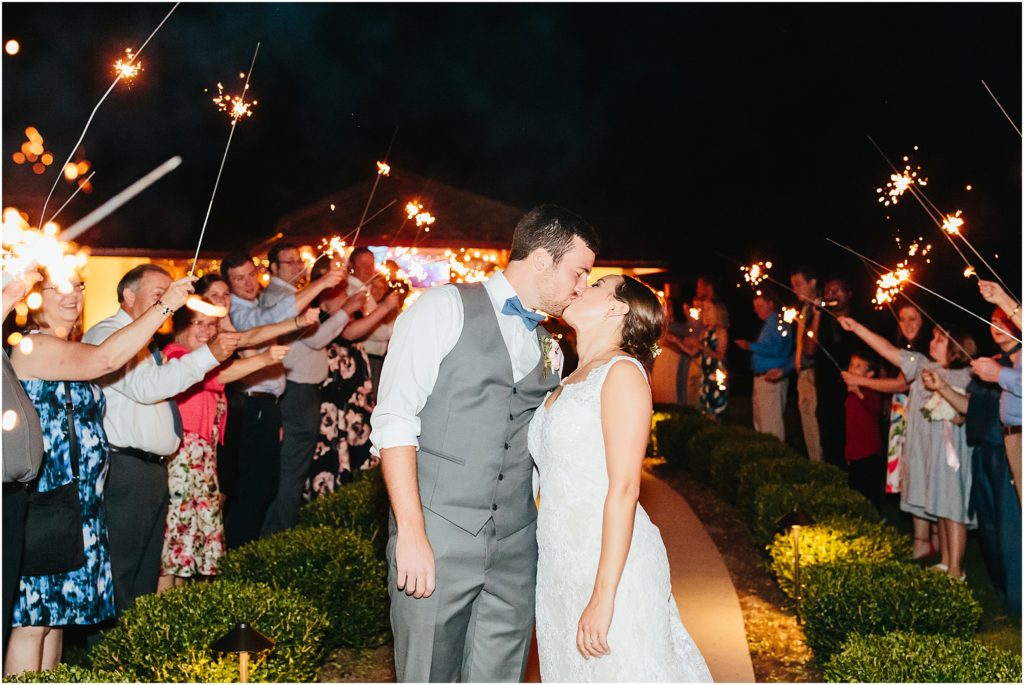 Couple kissing as crowd is exiting and sending them off with sparklers 