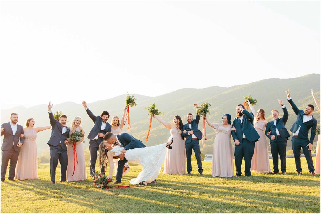 Bridal party cheer as bride and groom dip kiss during golden hour at crooked river wedding 