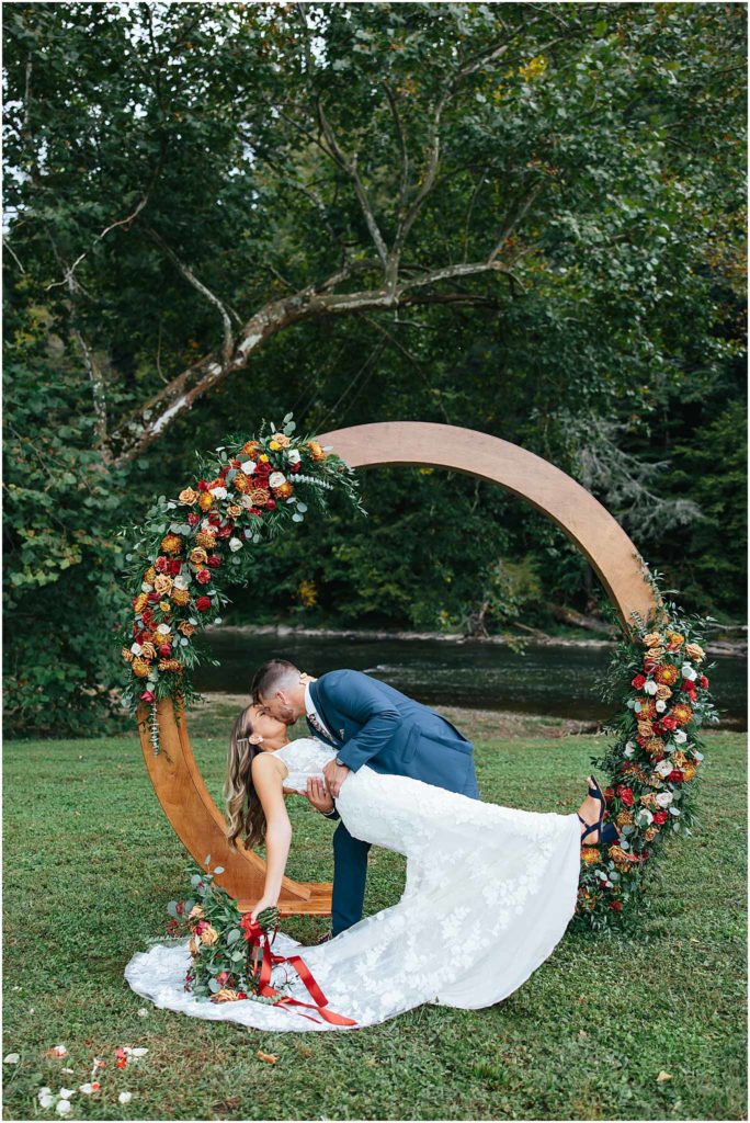 Couple dip kiss in front of flower arbor at crooked river wedding event 