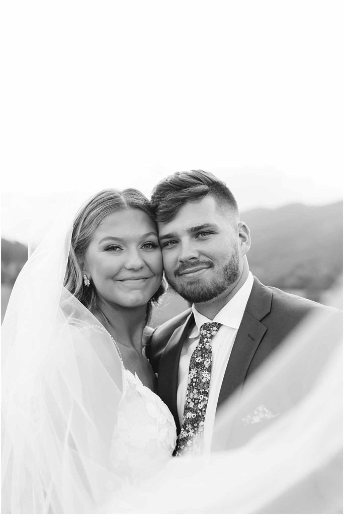 Married couple in black and white smiling toward photographer at crooked river wedding venue