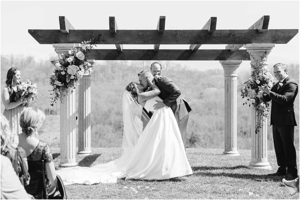 Bride and groom sharing first kiss in front of arbor at chateau selah taken by bristol va wedding photographers