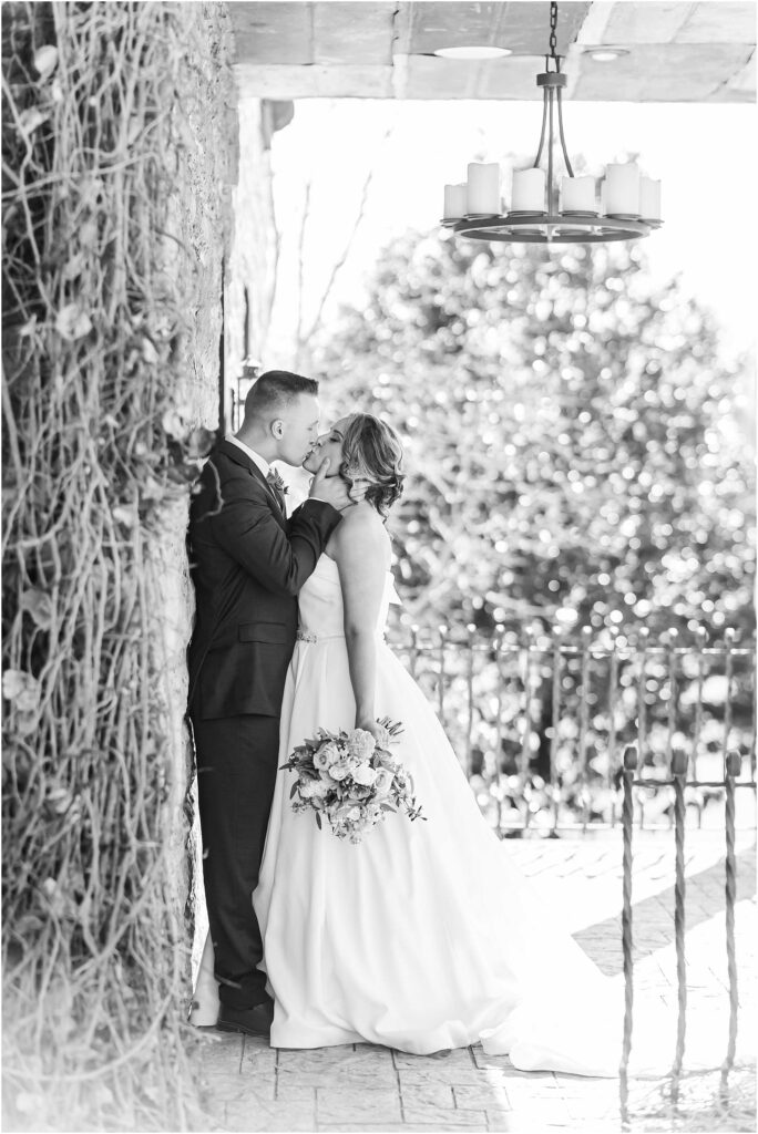 Bride and groom in black and white leaning against wall kissing with chateau selah in background