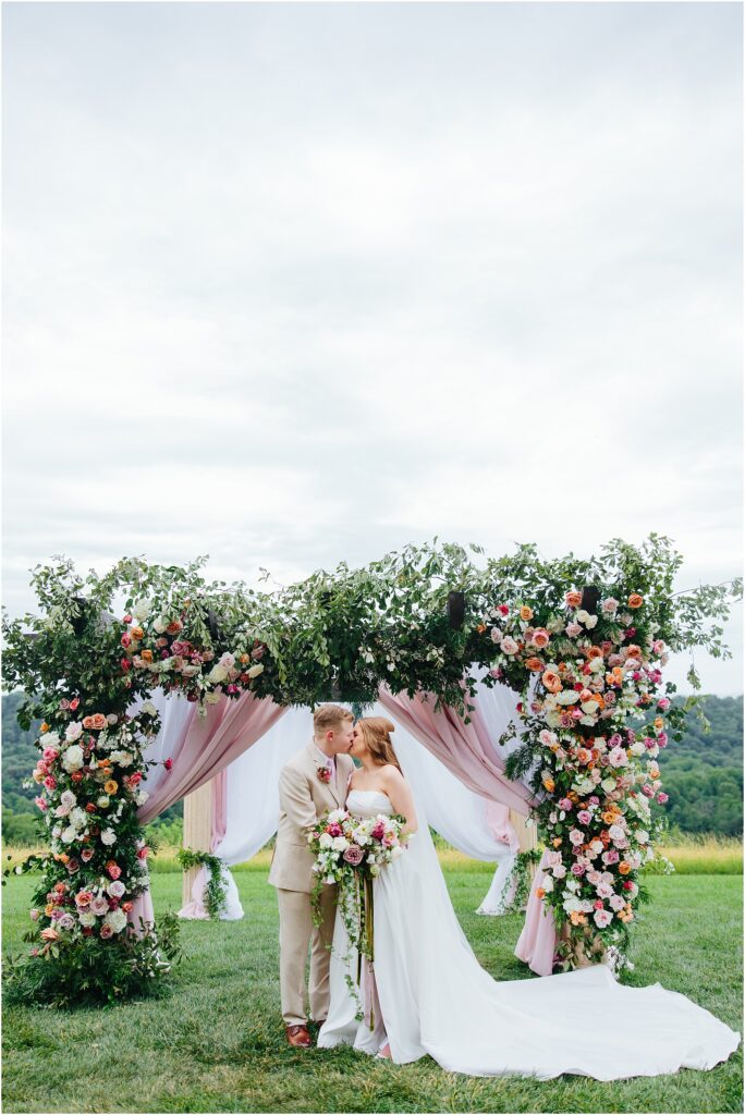 bride and groom share kiss in front of floral arbor at italian villa wedding blountville